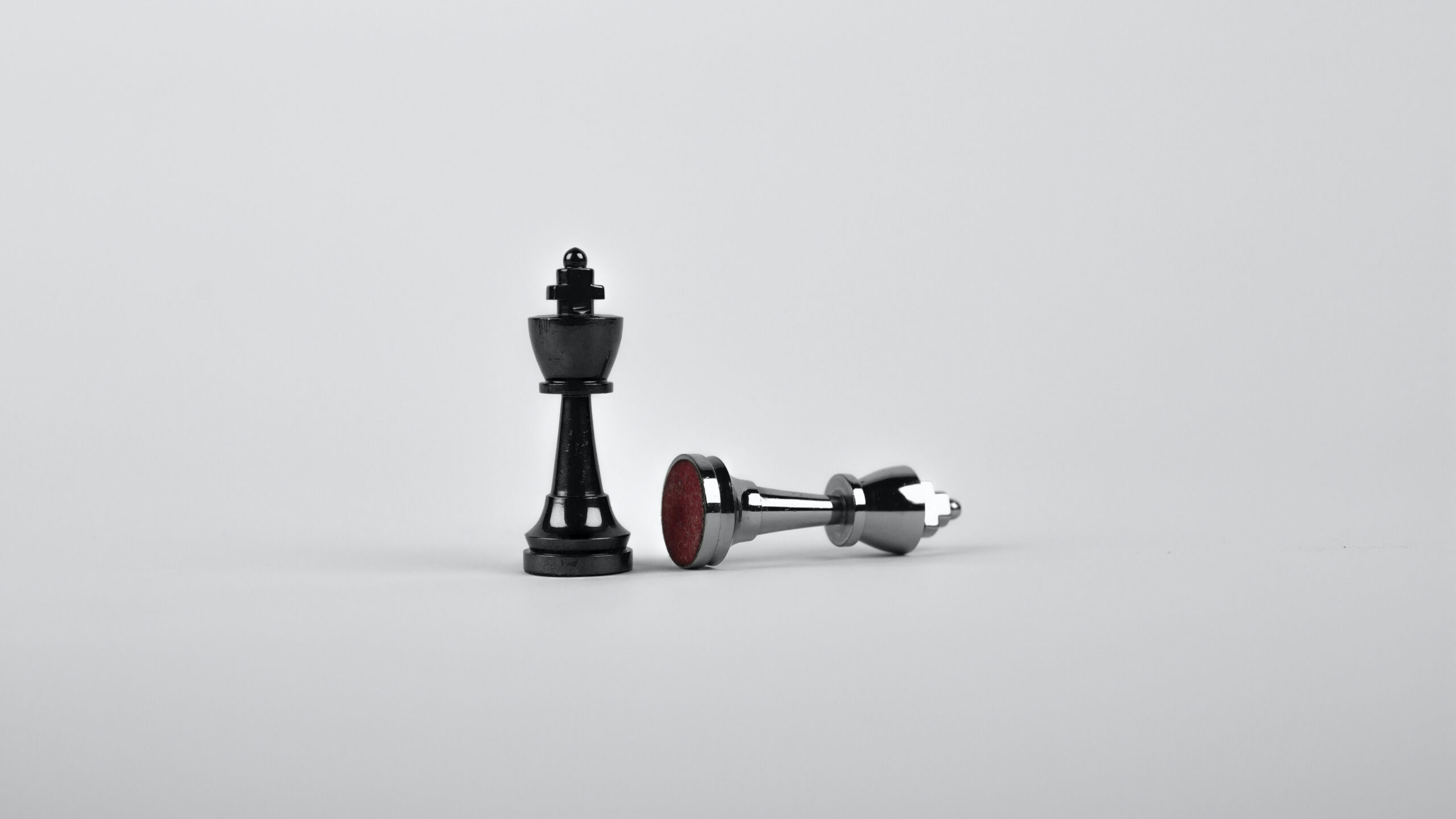 Two chess pieces in front of white background. Both are Kings, one is on its side, defeated.